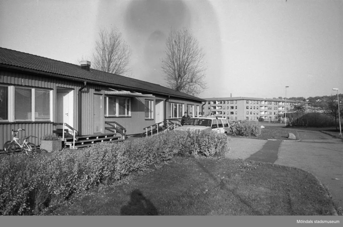 En utomhusbild på enplanshuset Katrinebergs daghem. Utanför entrén har någon parkerat en cykel. Längre bort står en man bredvid en Volvo kombi. I bakgrunden ser man Åbyområdets fyravåningshus med lägenheter.