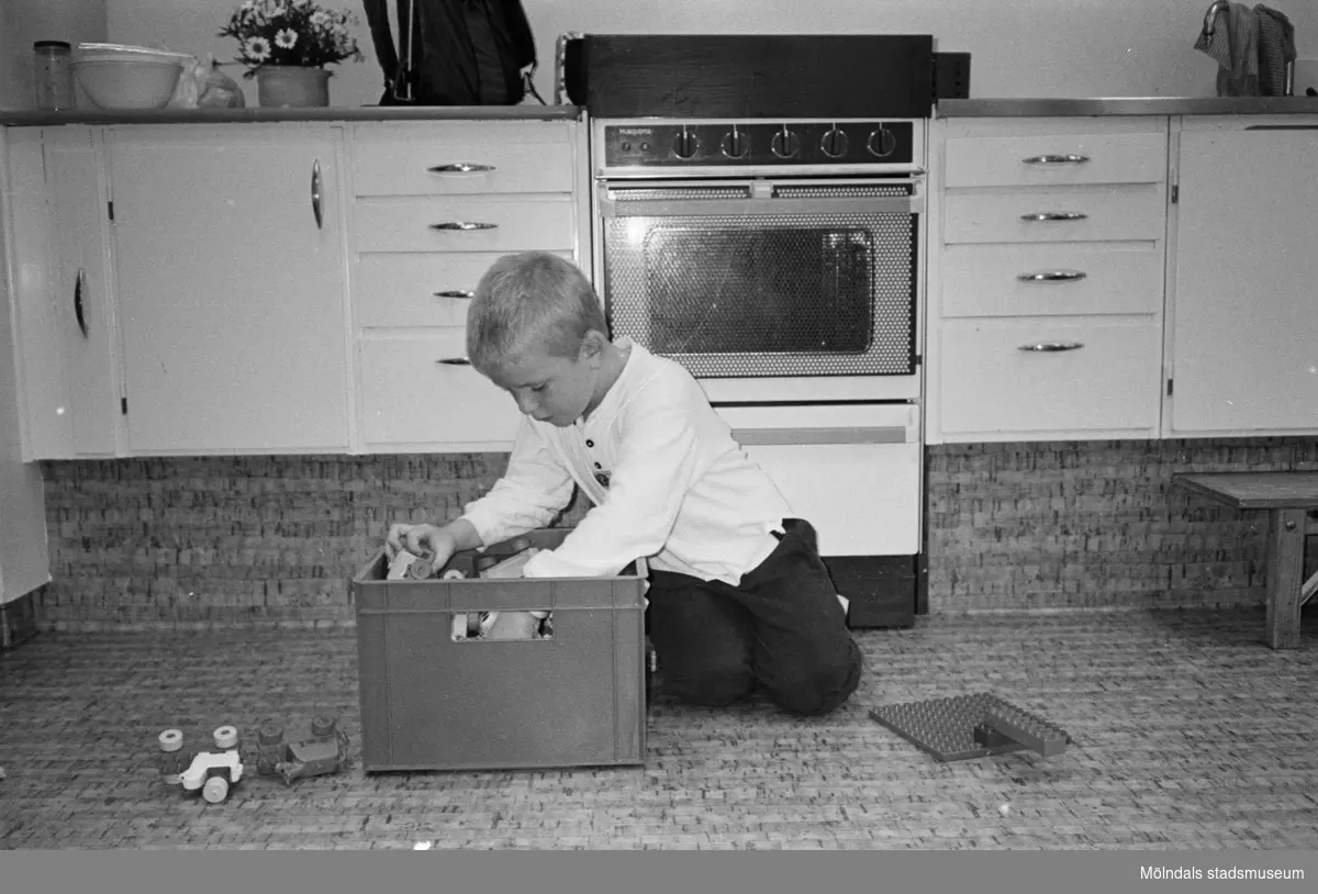 Pontus sitter på köksgolvet och letar runt i en plastback som är fylld med duplo-lego. En byggplatta och ett par duplo-bilar ligger på golvet. Hoppetossan, Katrinebergs daghem, 1992.