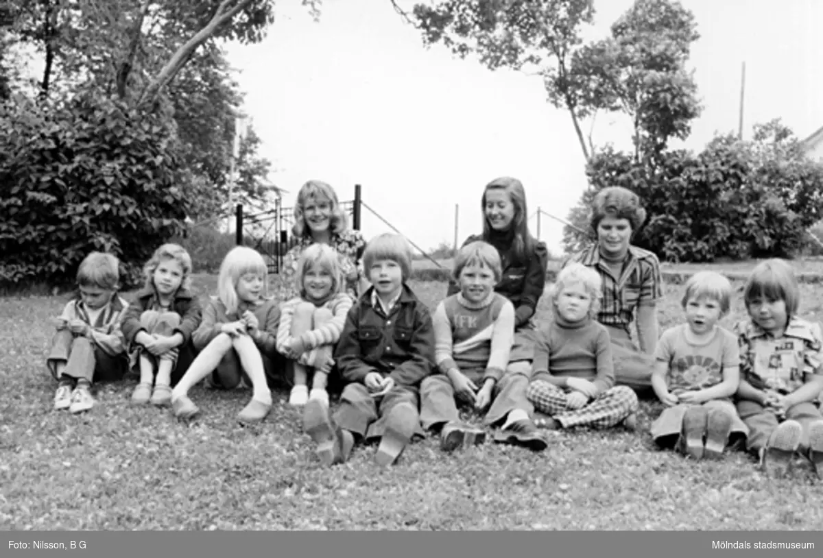 Några barn och tre fröknar sitter i gräset. Holtermanska daghemmet 1973.
