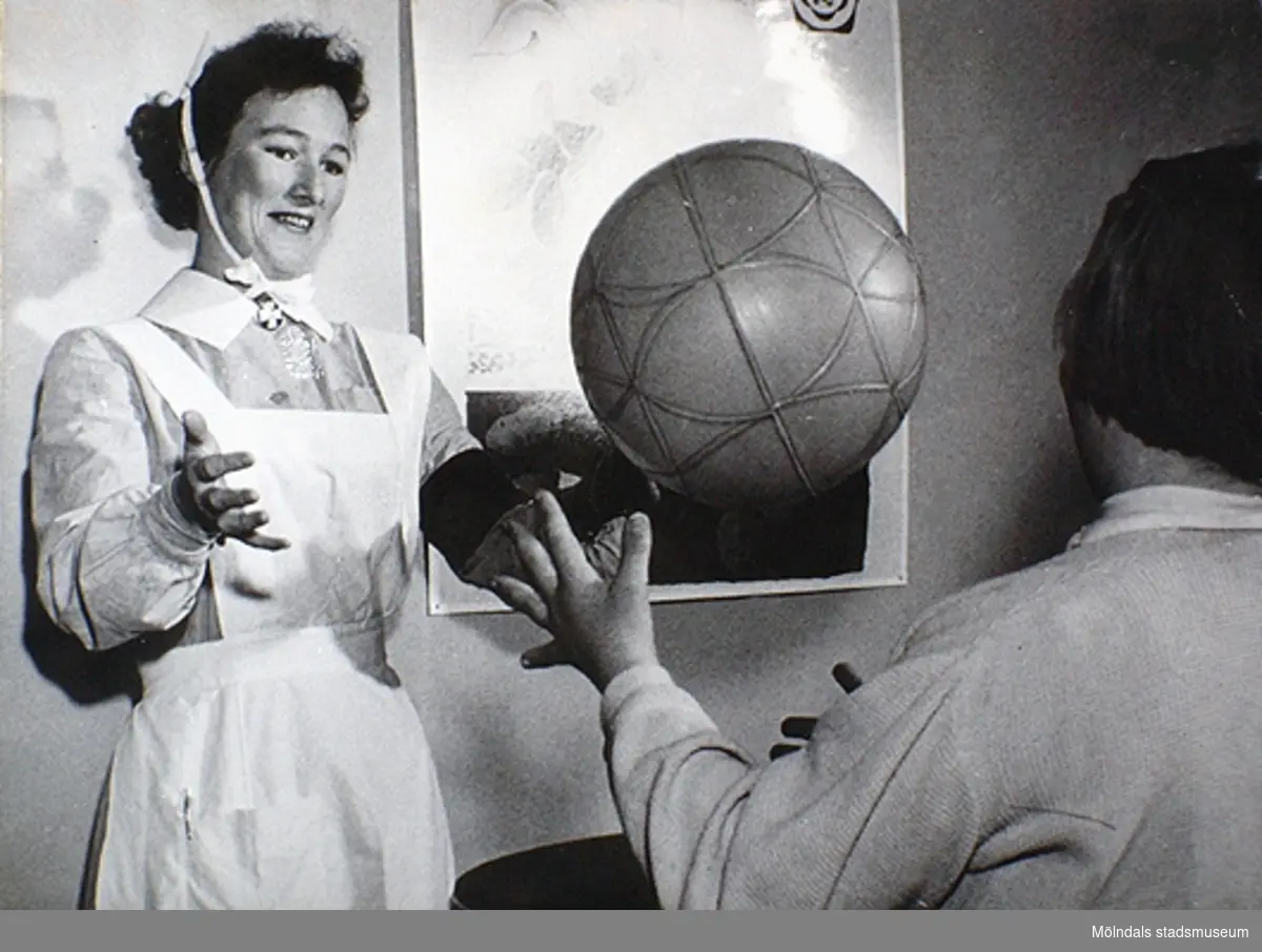 En sjuksyster som kastar boll tillsammans med ett barn. Under 1950-talet kom allt fler specialister, t ex sjukgymnaster. Okända namn och årtal.