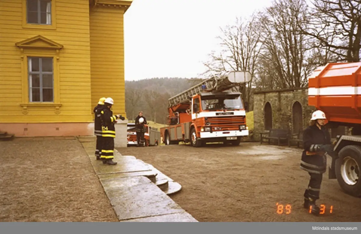 Tre brandbilar ståendes efter varandra utanför slottets västra sida. Även några brandmän står där.