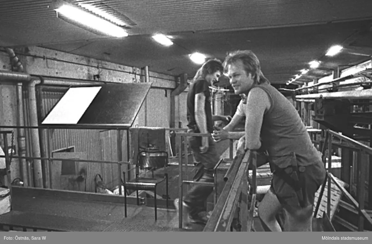 Två män i arbete på pappersfabriken.
Bilden ingår i serie från produktion och interiör på pappersindustrin Papyrus, 1980-tal.