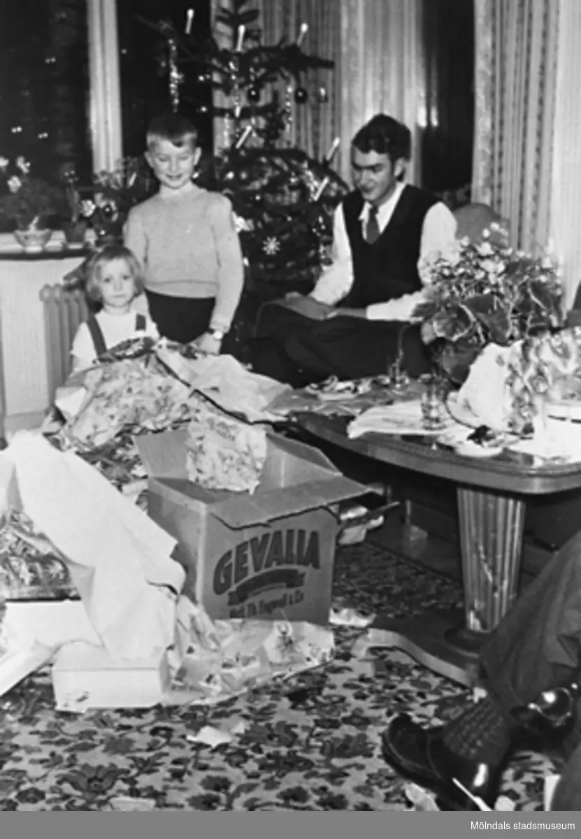 Två barn och en man öppnar sina julklappar vid granen. Okända personer, plats och årtal.