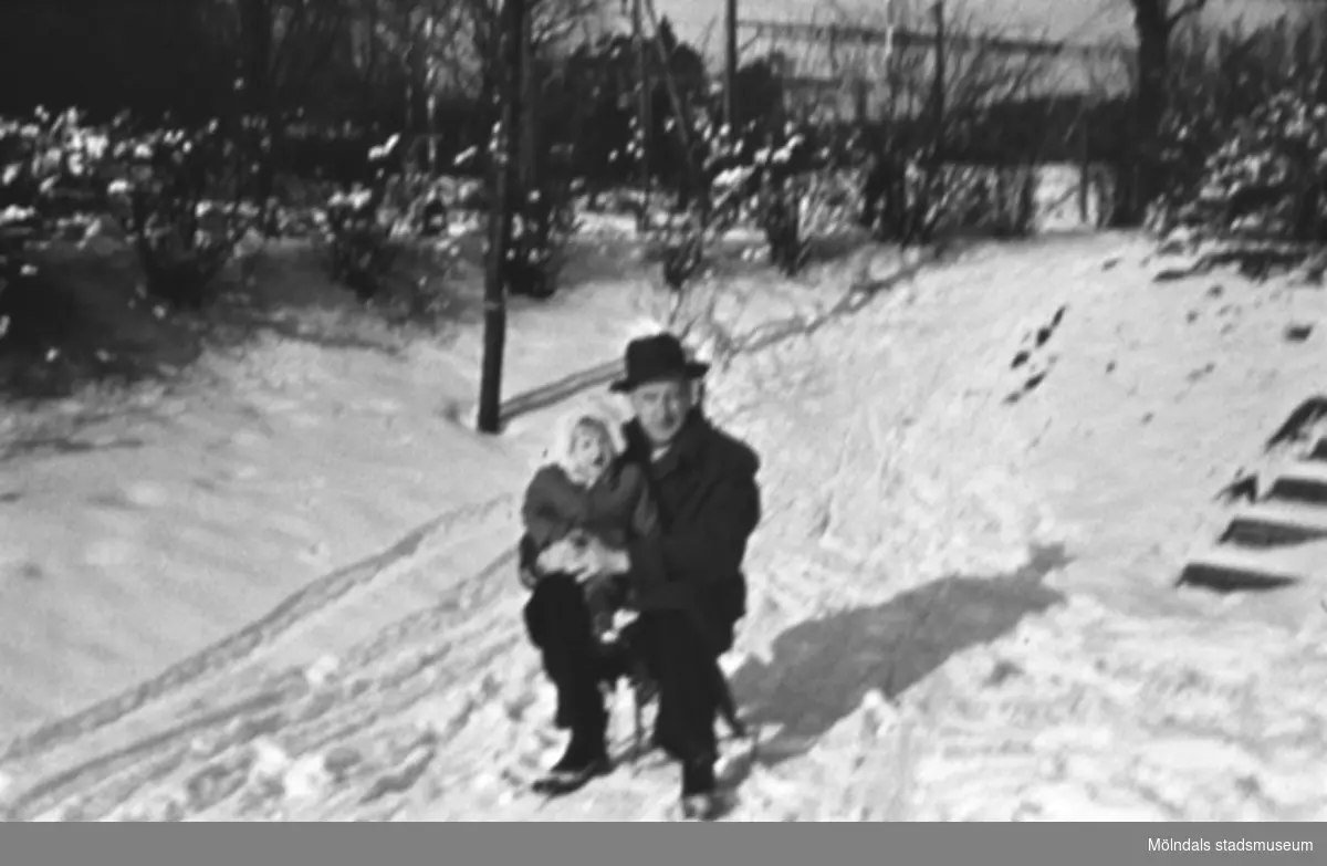Porträtt av en man och ett barn som sitter på en kälke i snön. Foto 1 är sv/v och foto 2 är i färg. Okända personer, plats och årtal.
