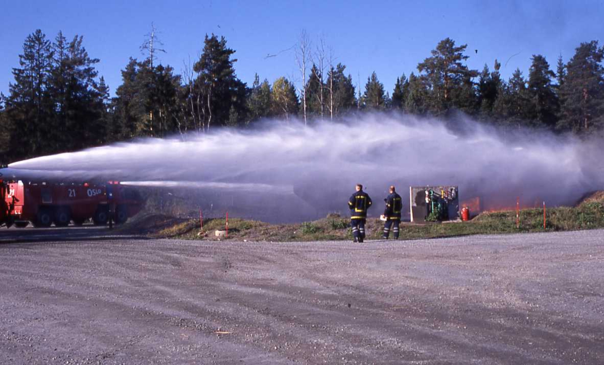 En rød brannbil spruter vann over "øvelse flyet" to brannmenn i front, fra gardermoen flyplass, OSL.