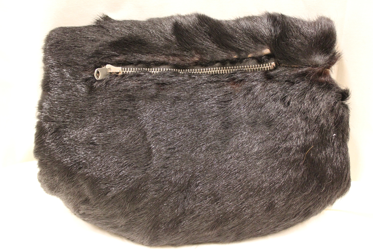 Muffe i sort minkpels med glidelås på ene siden for oppbevaring av feks. mynter. Har tilhørt "Gulovna Edwarda Giskedal" f.15.09.1885 - d.1977. Var gift med "Oluf M. Mydland"