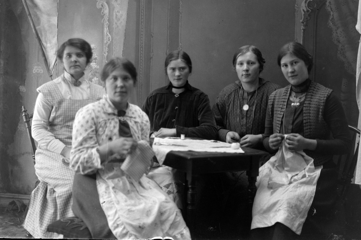 Studioportrett av fem kvinner som driver håndarbeid rundt et bord.