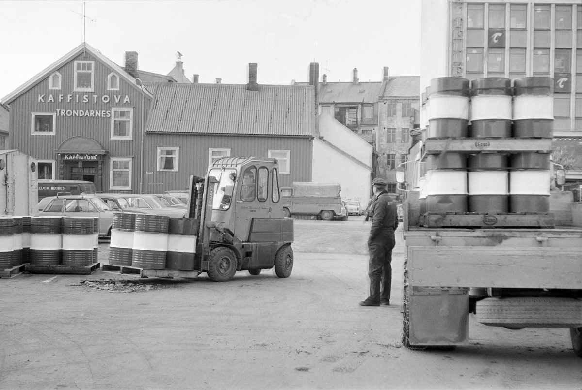 Gaffeltruck laster eller losser oljefat fra en lastebil. Bildet er tatt på dampskipskaia, vi ser Kaffistova i bakgrunnen.