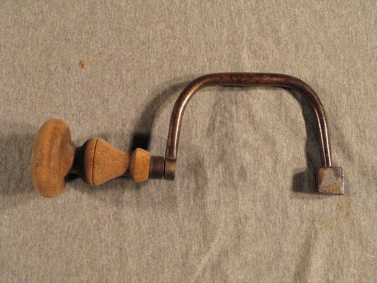 Form: U-forma jernstang med feste til bor i eine enden og påsett dreia treknapp til å halde og trykke i andre.
