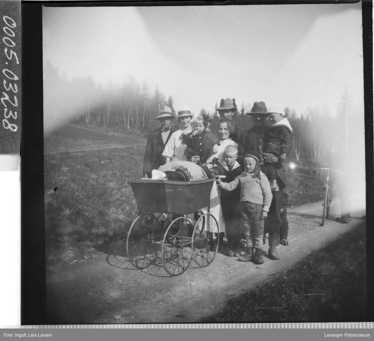 Gruppebilde av tre menn, to kvinner og fire barn ved en barnevogn.