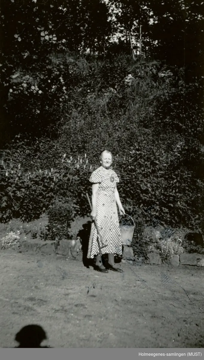 En kvinne med et redskap og en bøtte i en hage.