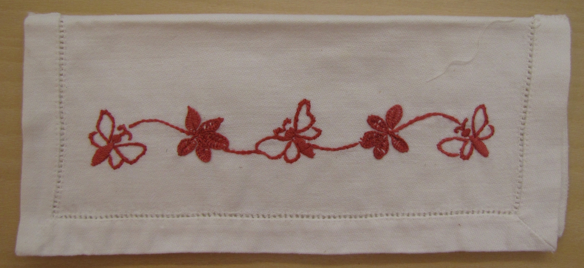 Väska för servett. Troligen tillhört någon av givarens mostrar (födda på 1890-talet).

Broderi i rött, fjärilar och blommor. Hålsöm runt kanten.