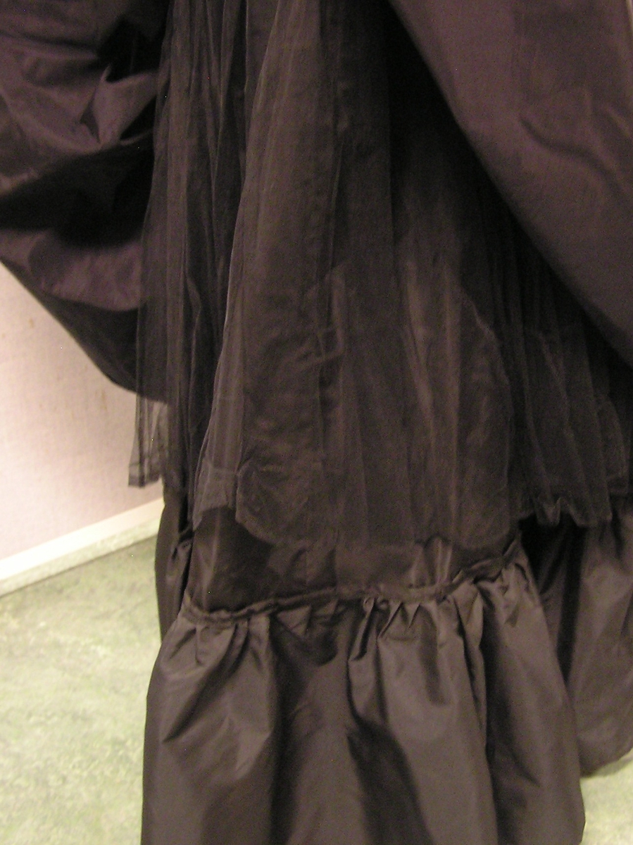 Gallakjole i to-deler. Enkel bluse med puff erme og rysje krave. Skjørt med bred linning, glidelås og hekte bak. Skjørt har tre lag. Kort skjørt øverst, underskjørt i midten og lang skjørt innerst. To sjal eller belter følger med. BKM.013423 og .013424.