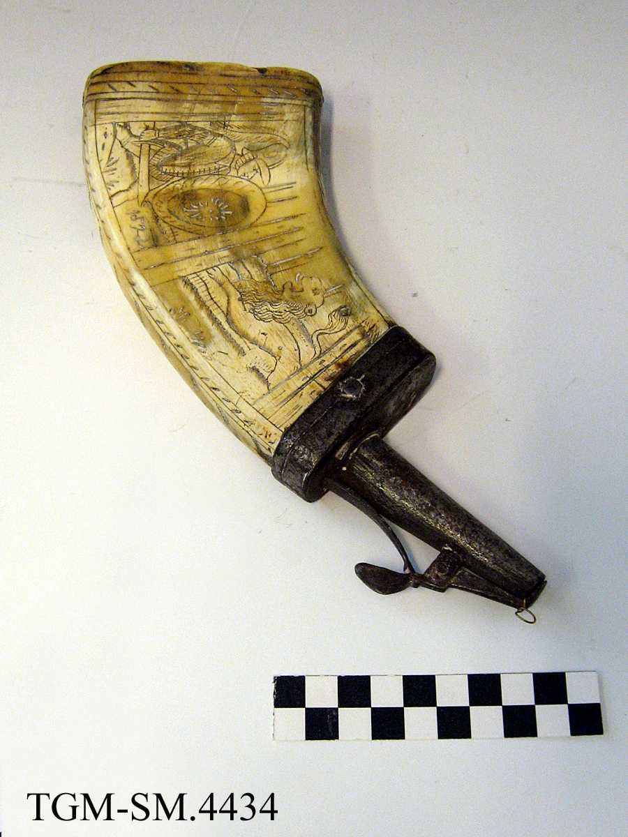 Fra protokollen: Fladt, med graverede billeder. Rimeligvis oksehorn presset fladt, firkantet. Træbund indfældt nederst, og ved den smalere ende jernbeslag med pipe som kan stænges og aapnes med en fjær. Aarstallet 1522 i det ene felt er muligens egte.
