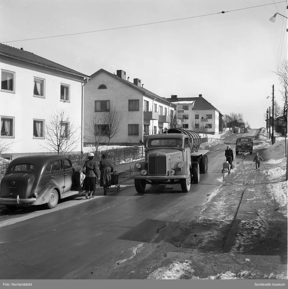 Efter en snörik vinter med sen snösmältning får lastbilar och bussar kryssa mellan gångtrafikanter och barnvagnar på Fridhemsgatan i trakterna av korsningarna med Vintergatan och Skogsgatan.