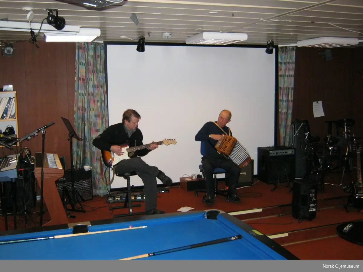 To musikere spiller gitar og trekkspill i kinosalen.