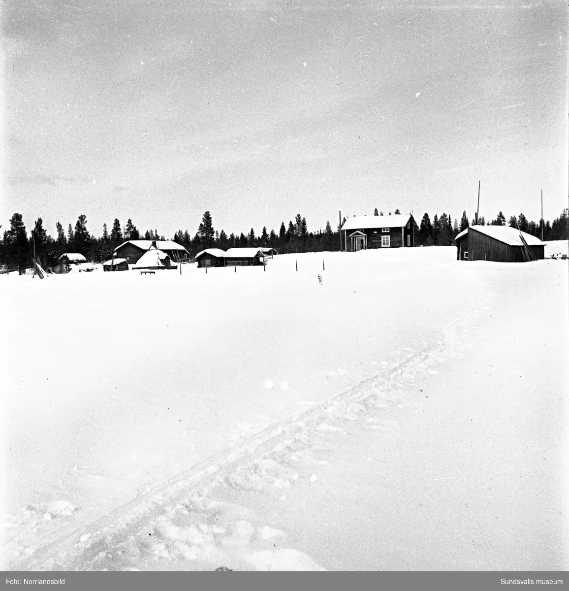 Vinterbilder från landsbygden, små stugor och uthus, barn som åker skidor, en kvinna står och handtvättar utomhus. Okänd ort.