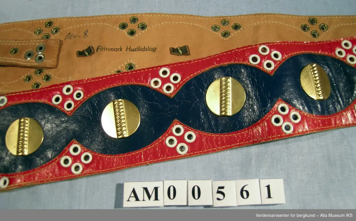 Belte sydd av rødt og blått skinn. Dekorert med 12 knapper av gullmetall og hvite maljer rundt.