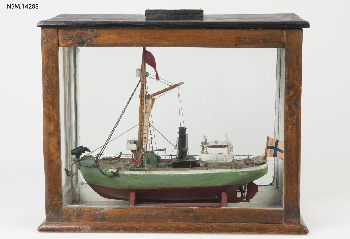 Enkel helmodell (sjømannsmodell) av hvalbåt i monter. Grønt skrog, mast, skorstein, 2 lettbåter, hvalkanon.