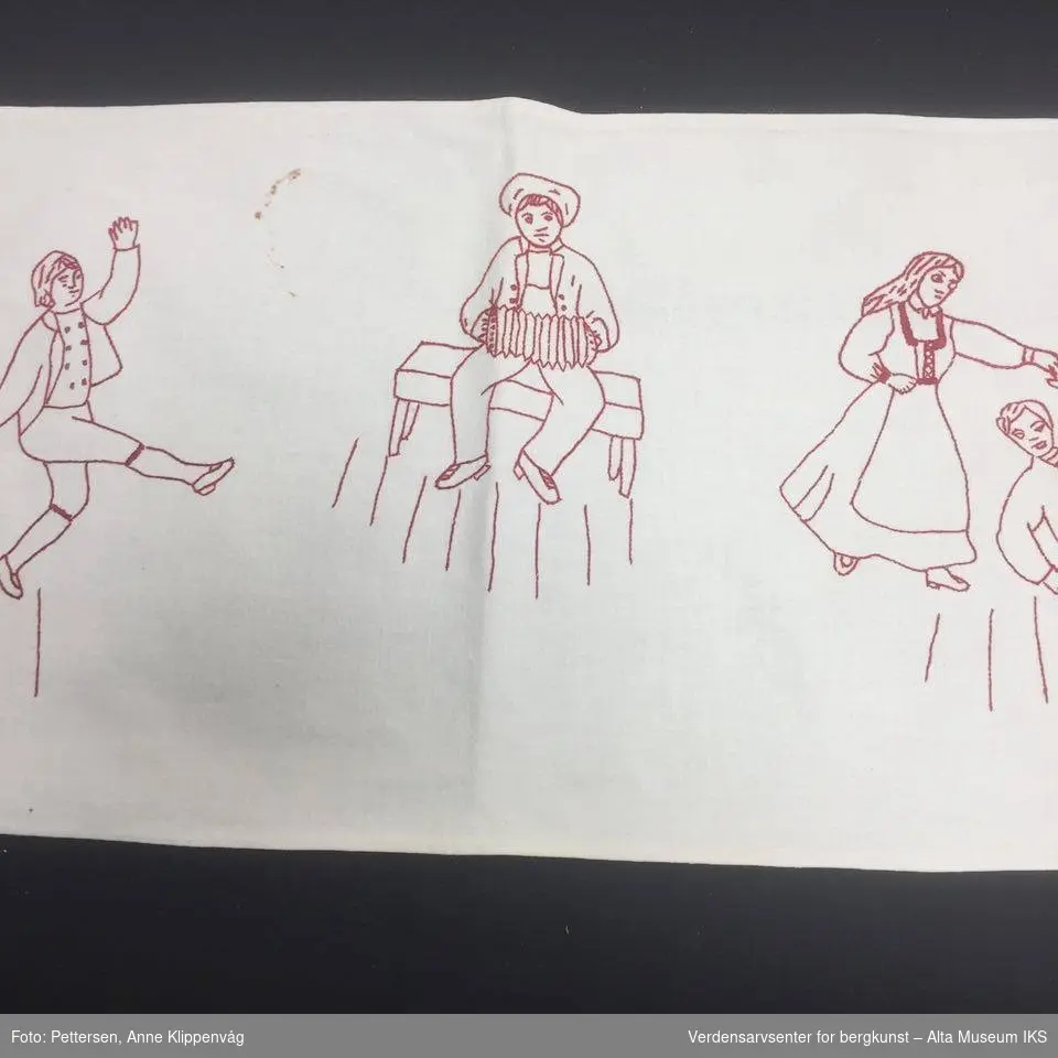 Rektangulært, hvit bordløper. Brodert motiv med rød tråd: En mann  som sitter og spiller trekskpill i midten, mellom to par som danser.