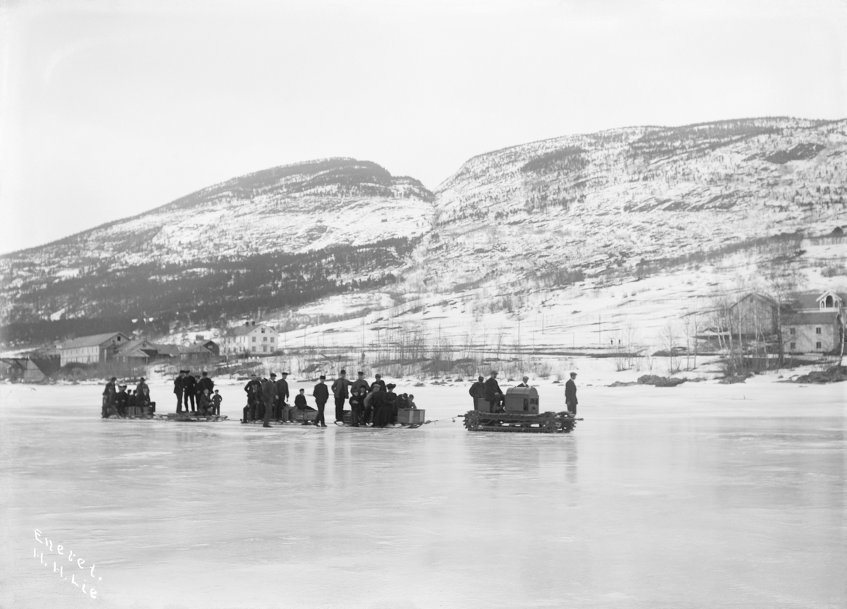 20.03.1910. Schots (Scott) motorslede. Motorisert beltekjøretøy, sleder med folk, islagt vann, bygninger i bakgrunnen.
