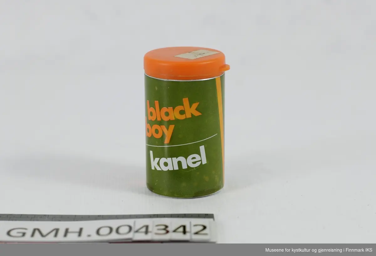 Den sylinderformede boksen er laget i metall og har en olivengrønn design med hvite og oransje bokstaver påtrykt. Lokket er av fleksibel, oransje plast og sitter på et fast lokk med strøhull i av samme material og farge. Emballasjen er tom.
