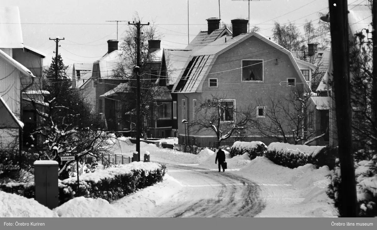 Rynninge 19 februari 1969

På en gata går en kvinna i jacka och med väska, och på  
marken ligger det mycket snö.