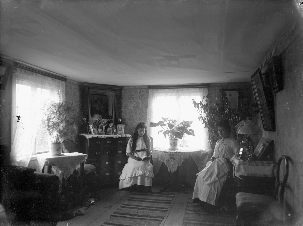 Rumsinteriör, två kvinna och en flicka, läsning och handarbete.
Salen på övre våningen vid gamla Norra Hyddan i Svennevad. De två flickorna är troligen Lilly Hallberg, född 1893 och Anna Hallberg, född 1896.