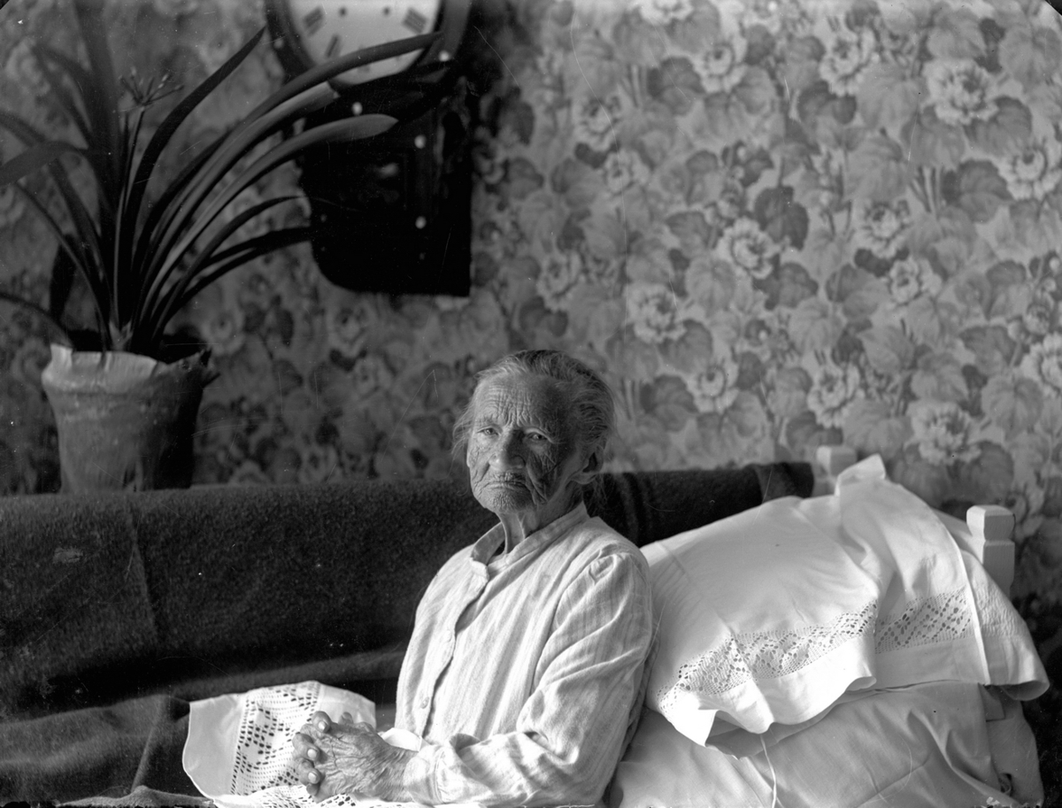 Rumsinteriör, en äldre kvinna i sängen.
Clara Gustava Gustafsdotter (född 1833-08-24) vid Kratorpsviken i Svennevad på 100-årsdagen.
(Sigrid Hallbergs farmor).