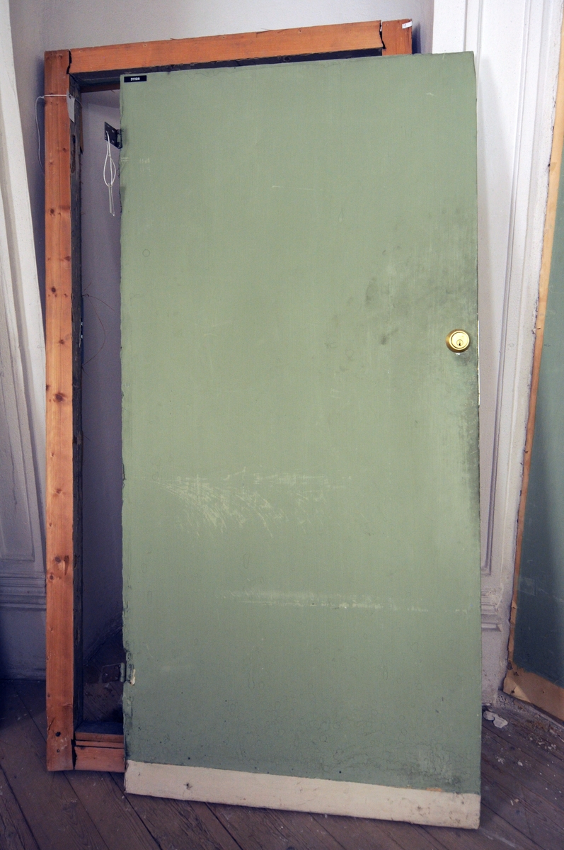 Karm med terskel. Dørblad med grønnmalt tapet på ene siden og hvitmalt med fylling på andre siden. Nyere lås.
