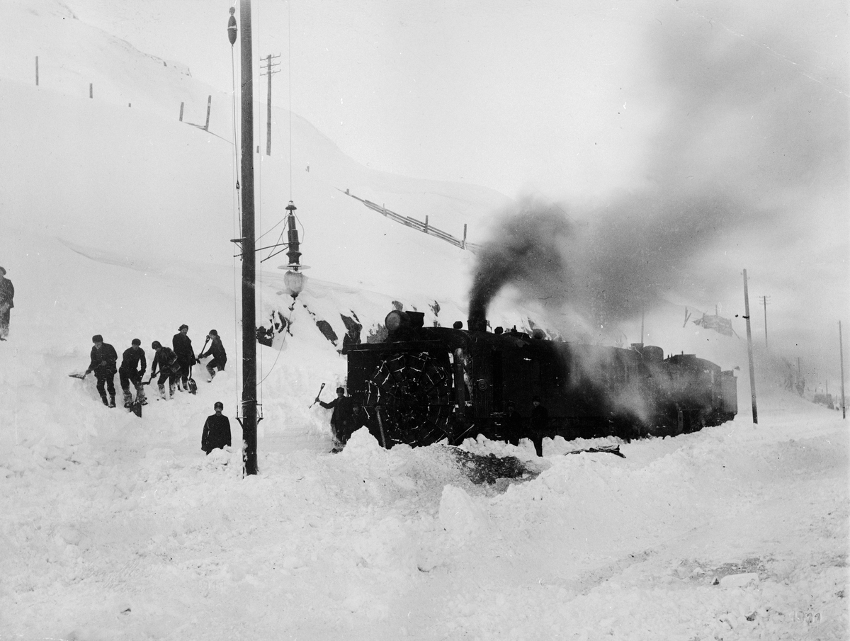 Vinterbild vid Riksgränsen. Män med spadar snöröjer för tåget.