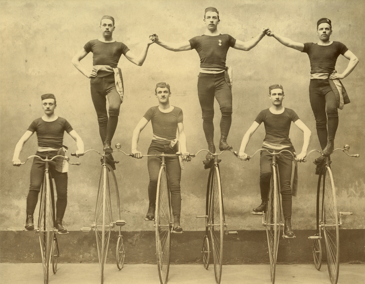Höghjulingar.
Stockholms Bicycle Klubb vid en uppvisning omkring 1885.
Byxor och tröja av trikå, snörkängor och blågult skärp var uppvisningsdräkten.