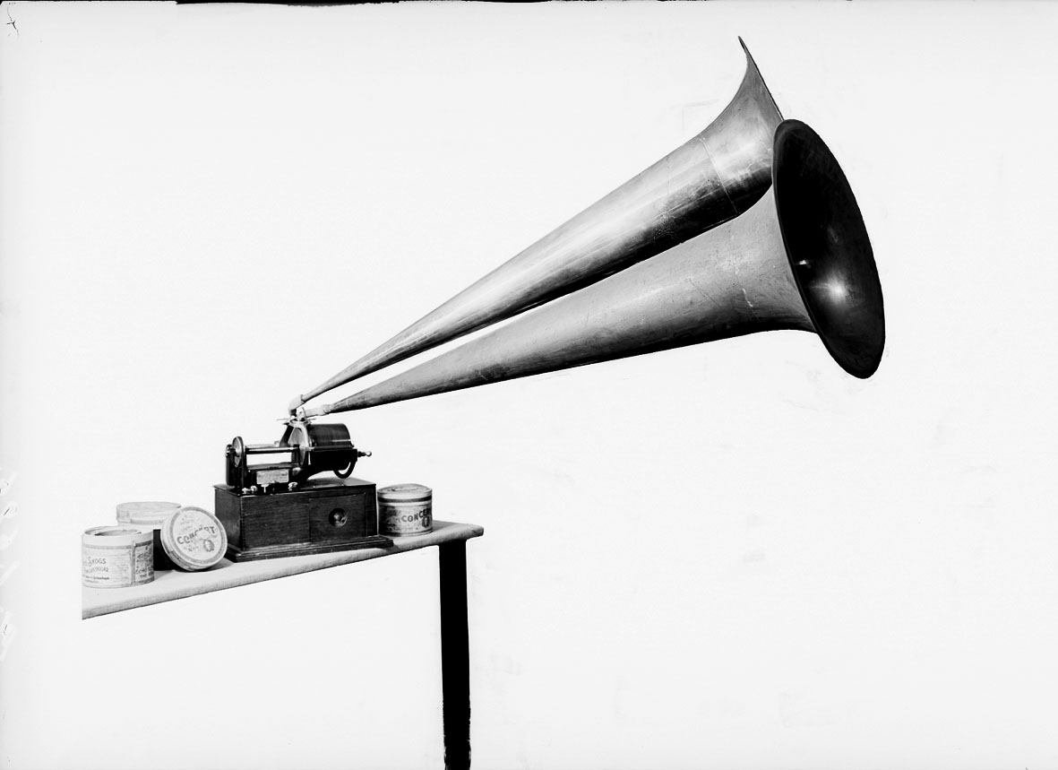 Fonograf, modell C, för "Grand" rullar enligt Edison, större typ med 2 synkroniserande ljuddosor och stora ljudtrattar av mässing. Märkt: Thomas A Edison. Orange Co. NJ.
Tillbehör: 23 st. vaxrullar (vilka saknas) för återgivning av musik (12 st. hela, 11 st. skadade) packade i 2 korgväskor, 2 st. ljudtrattar i fodral, 2 st. ljuddosor (extra), 2 gummislangar (bytta) samt 1 vev. Flätad konisk korg med lock (trattarna skall skjutas in i varandra).