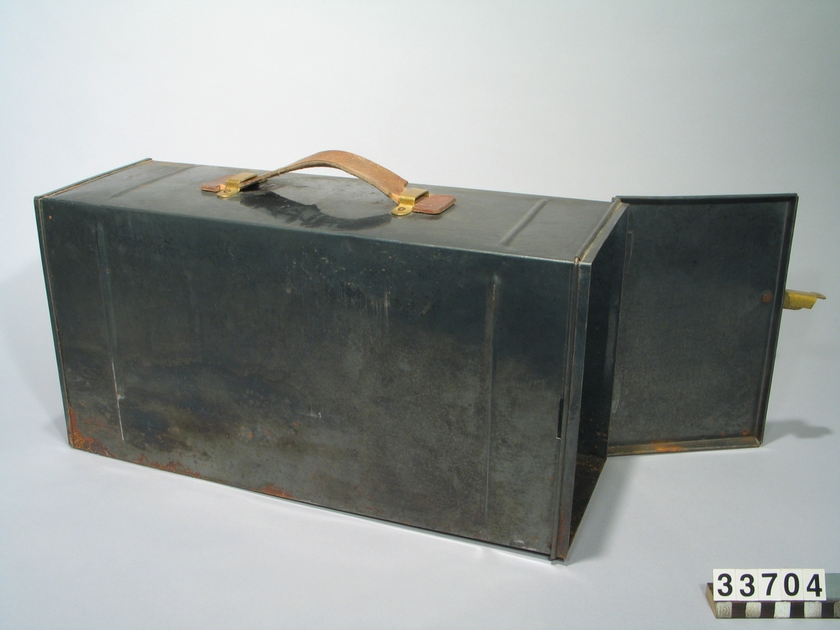 Förvaringslåda för skioptikonapparat enligt TM33702, av svartplåt med bärhandtag av läder och gångjärn i ena gaveln.