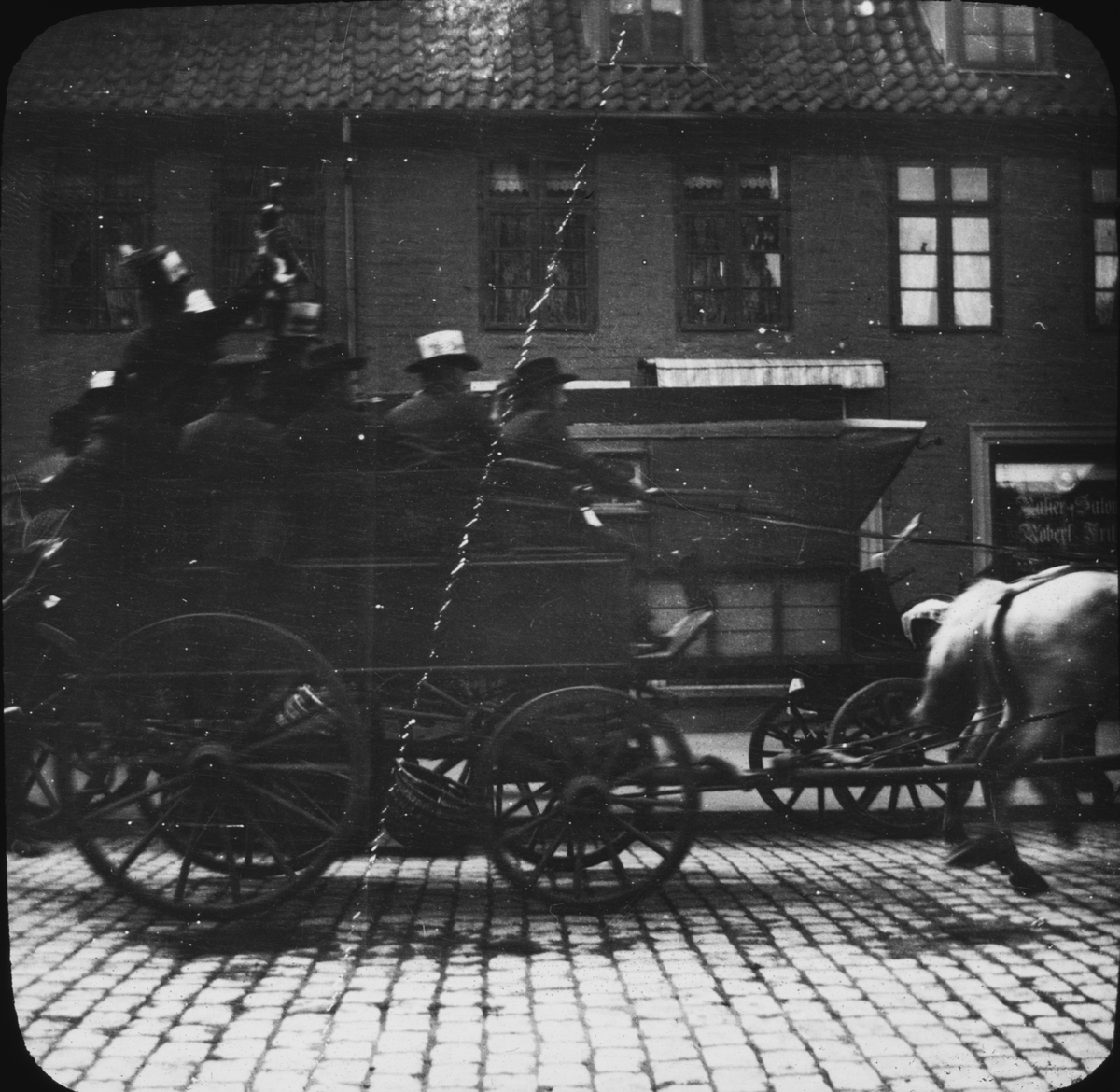 Skioptikonbild med motiv hästskjuts/ ekipage i full fart på gata i Lüneburg .
Bilden har förvarats i kartong märkt: Resan 1906. Lüneburg 8.