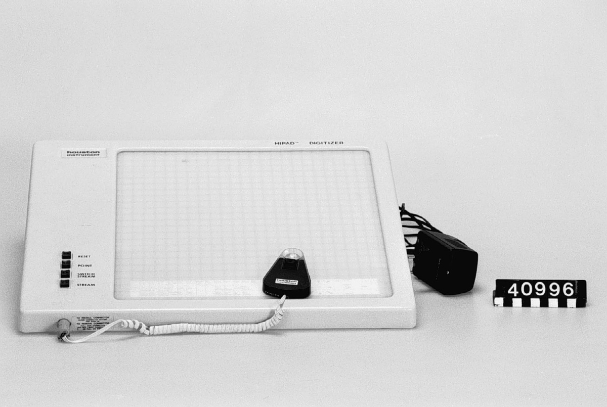 Pekdon för dator. Tillverkad av grå plast. Skiva av vit halvtransparent plast, indelad i ett rutnät. Styrdon (puck) av svart plast med hårkors, ansluten till bordet med en spiralsladd. Fyra knappar på ovansidan: RESET, POINT, SWITCH STREAM och STREAM. 25-polig D-sub och 3,5 mm phonojack i bakkant.