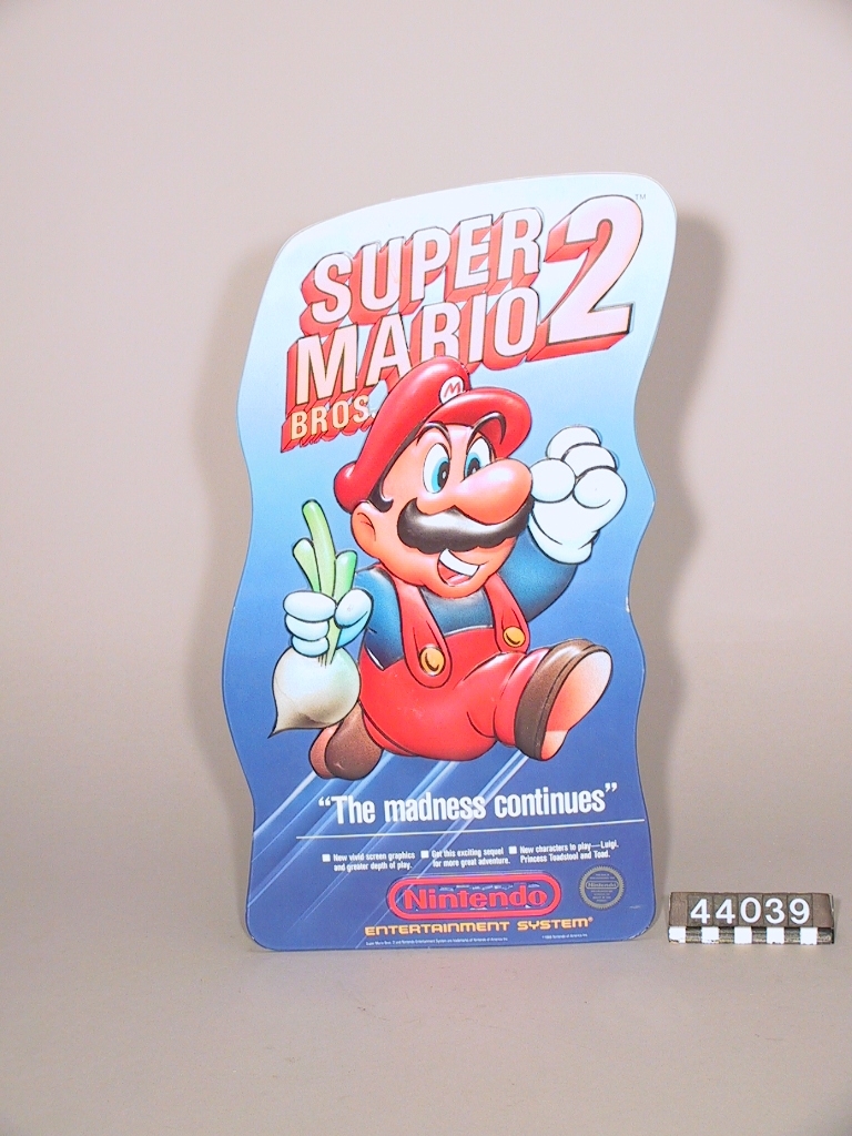 Fyra reklamskyltar: 1. Nintendo. Tillverkade av plast, svart och röd. Mått: 1220 x 320 x 60 mm. År 1987. 2. Super Mario. Tillverkad av papp. Röd/grön/blå. Mått: 690 x 500 x 2 mm. År 1987. 3. Super Mario 2. Tillverkad av papp. Mått: 470 x 260 x 2 mm. År 1989. 4. Super Mario 2. Tillverkad av papp. Mått: 70 x 500 x 2. År 1989.
