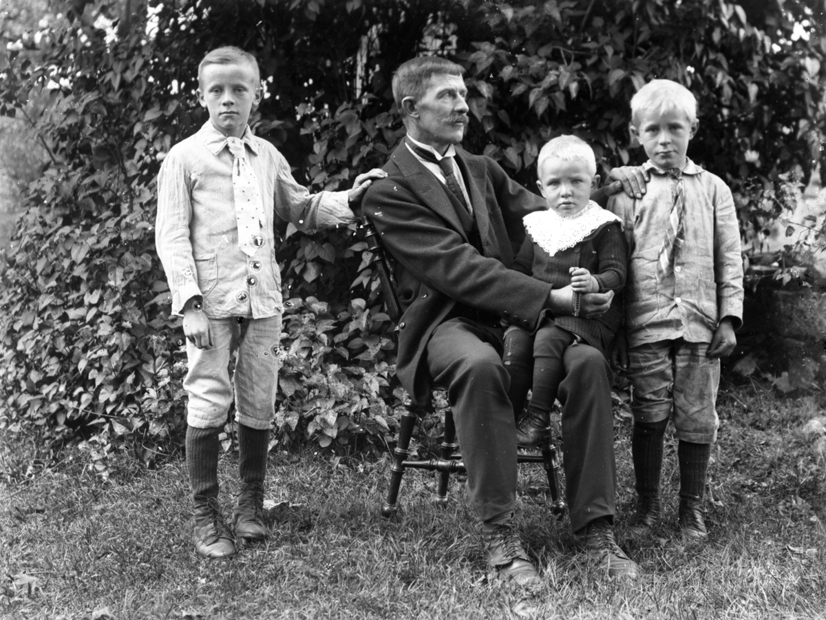 Familjebild. Far och tre söner  fotograferade i en trädgård.  Frans Larsson Ågården i Karl Gustav med barnen (fr vänster) Einar 1904-1971, i knät Verner 1913-2008 och Hilding 1908-1923.