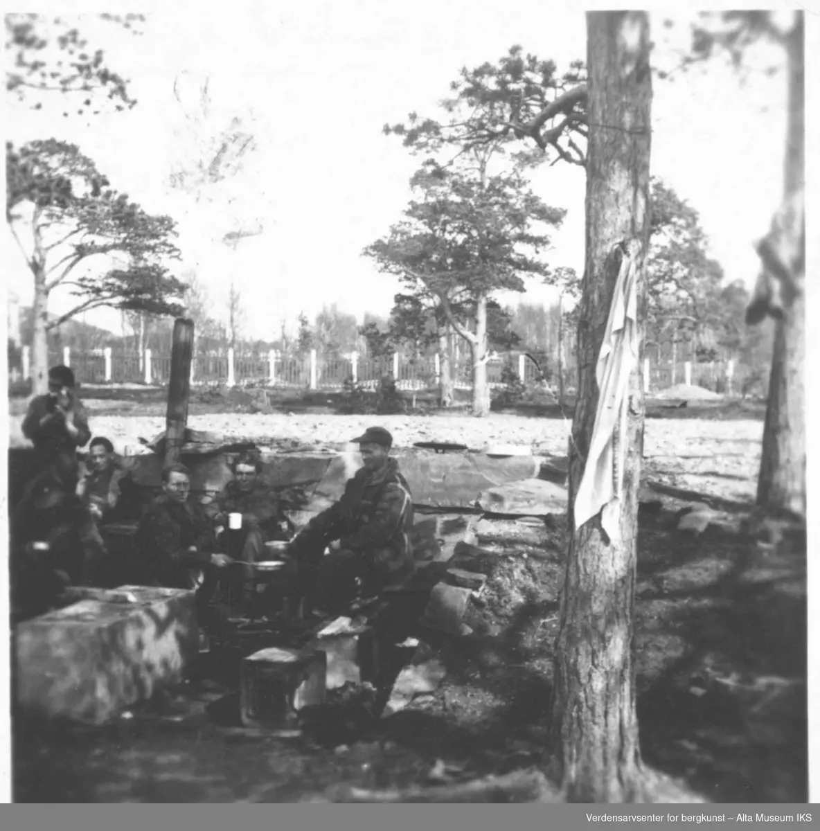 Soldater spiser utendørs under furutrær.
