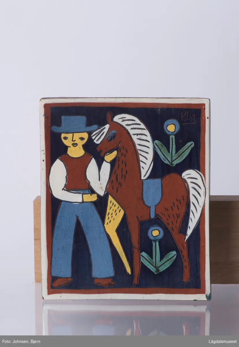 Motivet viser en mann med hest og blomster. Blå bakgrunn med brun og hvit kant.