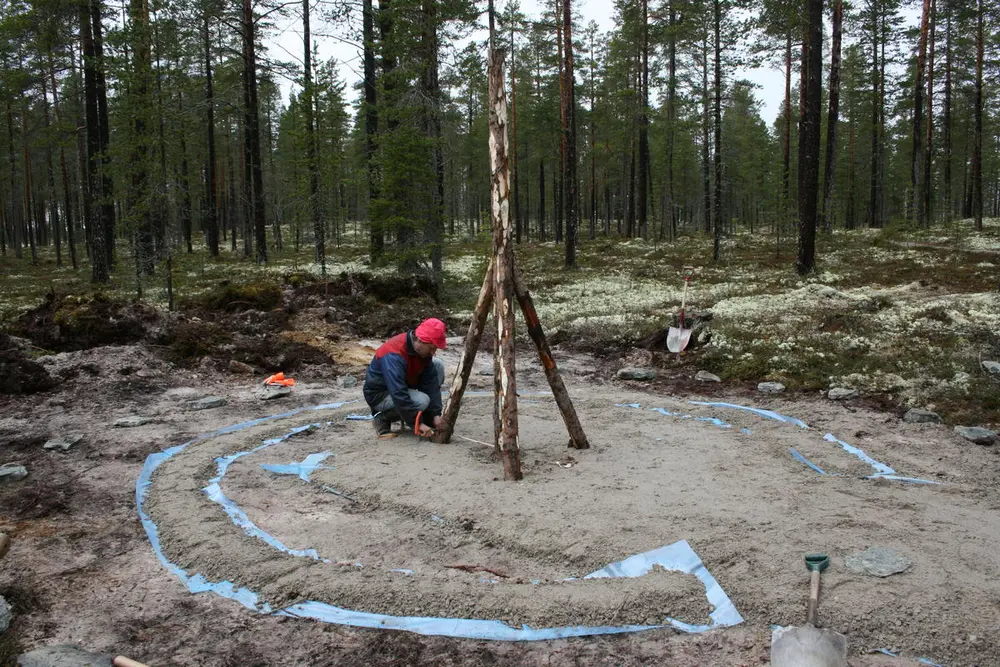 En mann utfører grunnarbeider til rekonstruksjon av kølmile. Det er lagt sand i en sirkel der kølmila skal bygges opp.