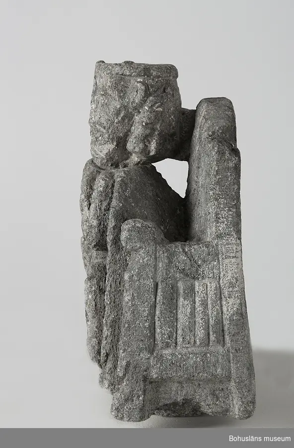 Stenskulptur av täljsten från Svarteborgs kyrka. Den helige Olof sittande i tronstol med högt ryggstöd. Han bär livbälte och mantel, en murkrona på huvudet, möjligen ett relikvarium i höger hand och håller vänster hand om skägget. Skulpturen är starkt eroderad.

Ur handskrivna katalogen 1957-1958: Olav d. helige, täljsten, Svarteborg. M: H. 41, största Br. 32,5 cm; krona och mantel, i höger hand spiran, vänster griper om skägget; sittande på en tronstol m. armstöd och högt ryggstöd, på alla håll smalnar stolen av uppåt. Starkt sliten.

Ur Katalog 1. Uddevalla Museihistoriska samlingar, svenska avdelningen. A. Yngre föremål. Upprättad av Knut Adrian Andersson 1916:                                                                                                                              No 34. Bild i täljsten av Olov den Helige. Yngre medeltiden, räknad till 1550. Förvarats i Svarteborgs kyrka under namnet "Kung Rane". Skänkt av församlingen år 1860-70-tal till Uddevalla museum. Förvaras ovanpå Medeltidsskåpet i sydvästra rummet.

Presenterad i  Uddevalla Museums tryckta katalog 1869 under rubriken 
F] Saker från yngre Medeltiden, räknad till 1550.
N:o 1. Bilder af S:t Olof i sten från Svarteborgs kyrka.

1861-1870 1 Arkeologiska och Etnografiska samlingarna U-a Museum D4A 1
Ur Gåvobok1864:
Svarteborgs församling:
Kristusbild af träd samt fragmenter af en Granit- [överstruket] Täljstensbild, enligt sägen föreställande Kung Rane, hvilka begge setat [överstruket] [oläsligt tillägg] i Svarteborgs kyrka. 
Tillagd kommentar av intendent Knut Adrian Andersson; Olof d. Helige troligen.

Se foton på föremålet i Uddevalla museums kyrkliga utställning 1920, UMFA54467:0089.
Tillstånd, se Vårdblankett.