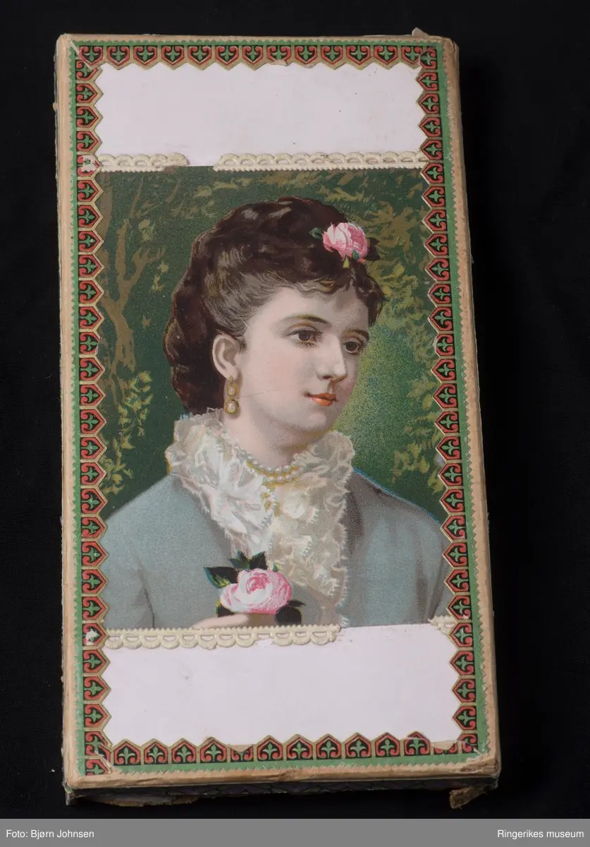 stiliserte blomster på en remse med en tungekant.  PÅ B - lokk: avbildet kvinne pyntet med blomster, perler  og en tett kant av blonder rundt halsen.