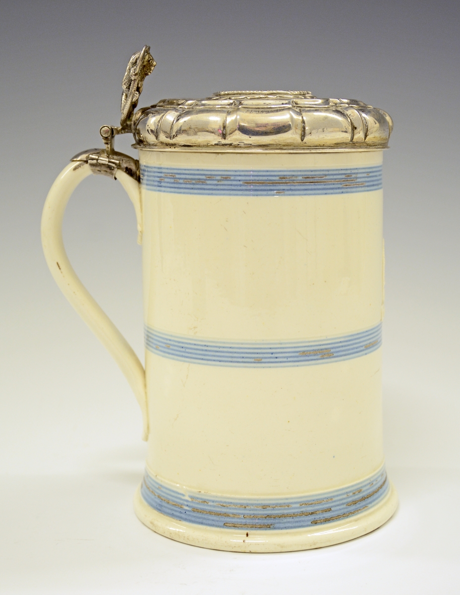 Fra protokollen: 
Steintykrus med sylvlok. Kruset sjølv cylindriskt med 3 blaa, rundu belte paa den kvite glasuren. Framme eit upphøgja felt i eggform med eit tverband yvi med stempla: CR-IV IMPERIAL.
Loket med støypt ciselera løve (med øks i labbane) til lokknapp og uppdriven runding i midten med innfelt sylvpening (medalje merkt F.3, 1659, arm fraa sky høgg av hond som grip etter ei krune). Voluten ikringum bytt med knekkir, og flaten rundt peningen med uppdrivne ciselera granne bandknekkmynster paa mattera grunn. Regence-stil; truleg arbeid av ein bygdesylvsmed (utan stempel). Paa volutknekkine er gravi einstad J. V. B., einstad M. H. D. H. og 1735. Høgd med loket 18,5 cm, tvermaal paa loket 11 cm. Stemp: CM.