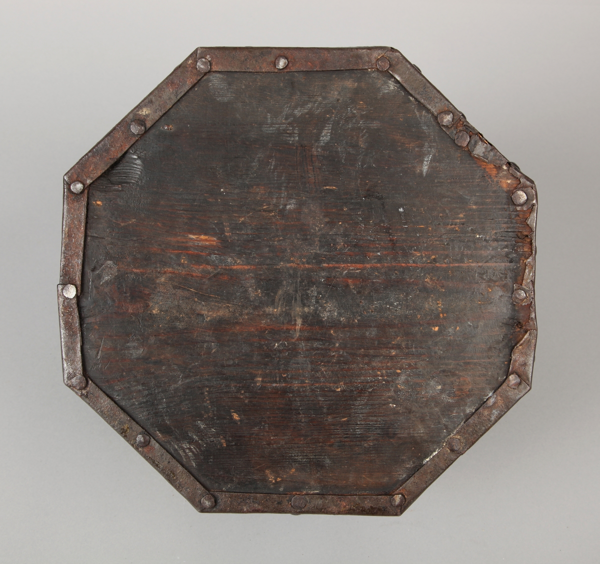 Åttekantet. Den har dekorerte flater i messing med jernbeslag og det hele er naglet på tre. På lokket er det en hank. Flaskefôret er låsbart, men den originale nøkkel mangler.