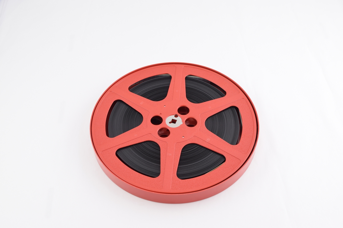 Filmrull i eske. Film på rød plastikkspole. Rødt rundt etui med rund grønn etikett.