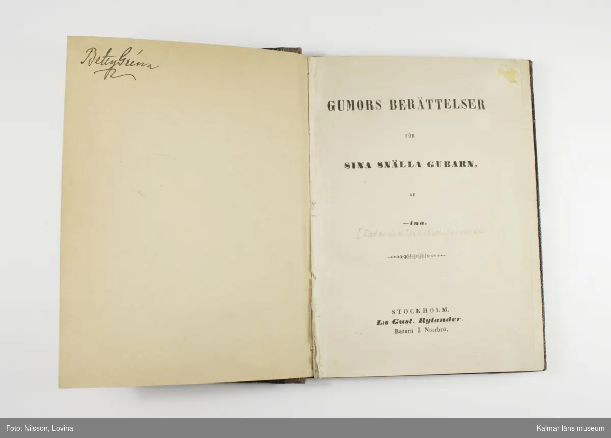 KLM 28703:20. Bok. Inbunden bok med titeln Gumors berättelser för sina snälla gubarn. Brunt omslag med text i guld. På första sidan står inskrivet: Emma Broberg.