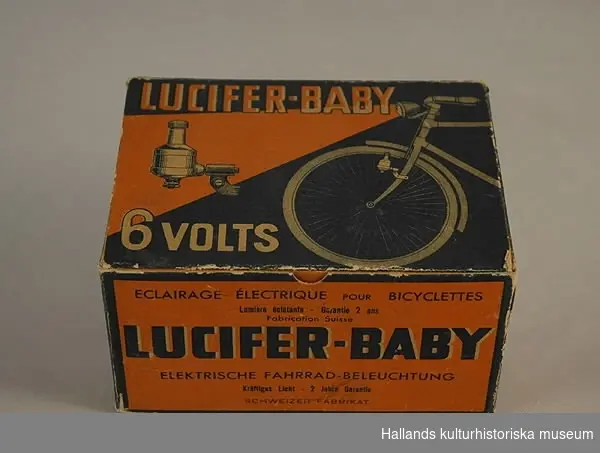 Svart och orange hopnitad pappask för cykelbelysning. På kartongen är framdelen av en cykel avbildad. På insidan av locket står en text skriven med blyerts.
