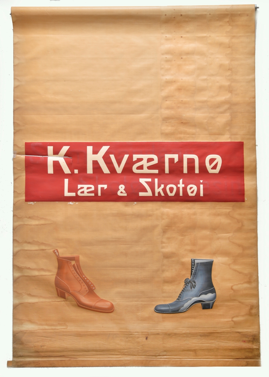 Rødmalt rektangulært felt med hvit påskrift "K. Kværnø Lær & Skotøi" plassert cirka midt på gardinen, under denne to påmalte sko(støvletter) vendt mot hverandre; den venstre brun (uten lisser) og den høyre tofarget mørke- og lyseblå (med lisser).