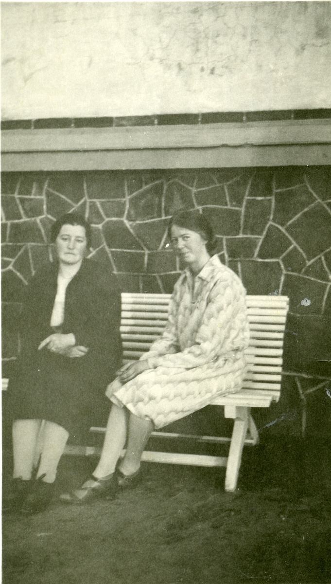 Portrett av to kvinner sittende på en benk.